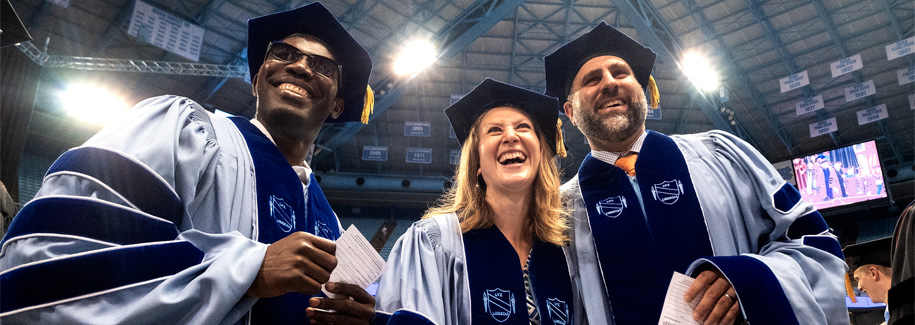 Three doctoral graduates wearing Carolina blue academic regalia smile as they celebrate their graduation.